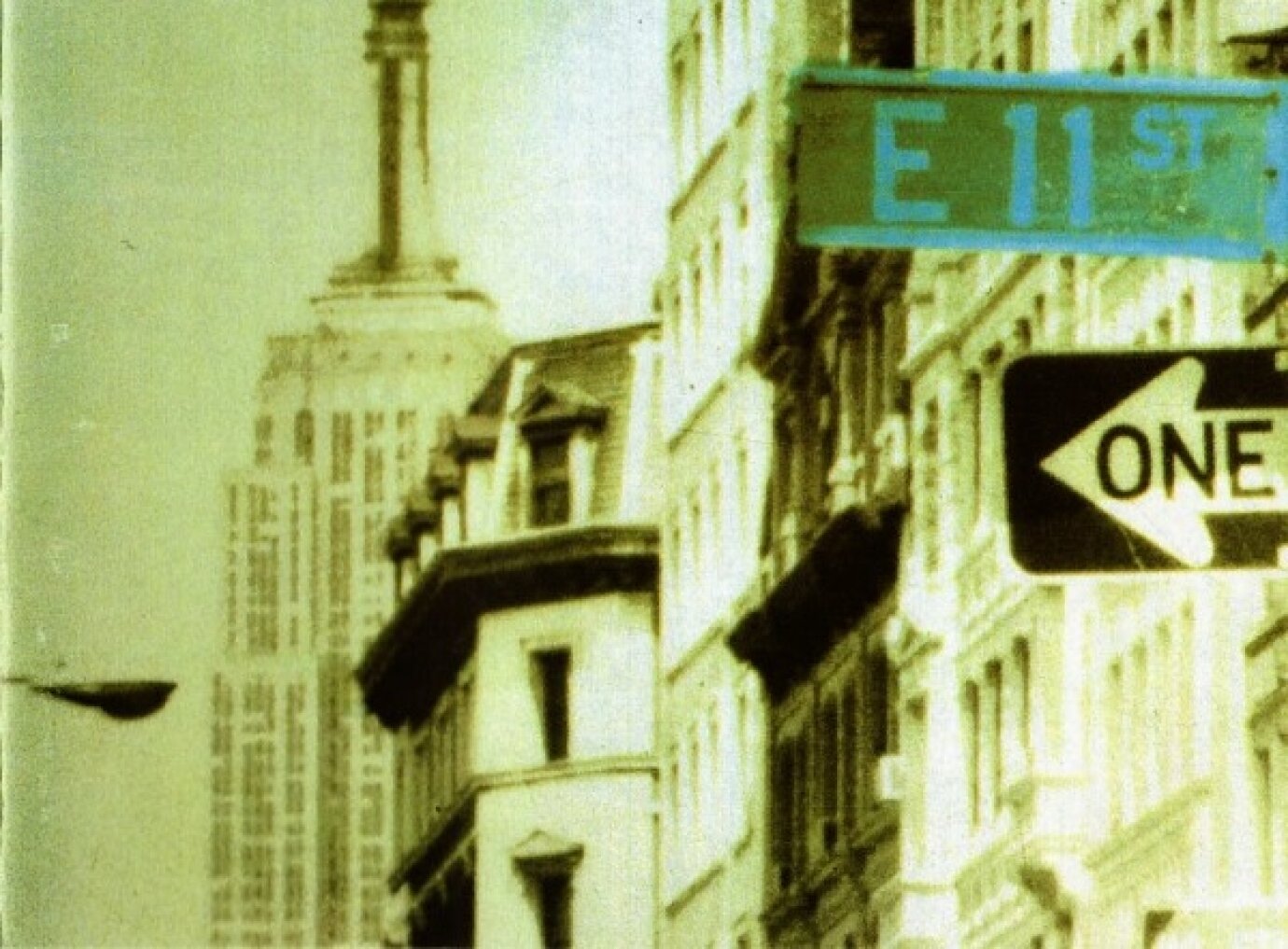 Alter, körniger Ausschnitt einer New Yorker Strasse mit dem Strassenschild «E 11 St» und Hochhäusern im Hintergrund